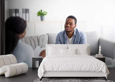 Effective psychotherapy. Young black guy talking to psychologist, receiving professional help at mental health clinic Wall mural