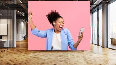 Enjoy The Music. Portrait of happy black girl listening to music with earphones and dancing over pink wall Wall mural