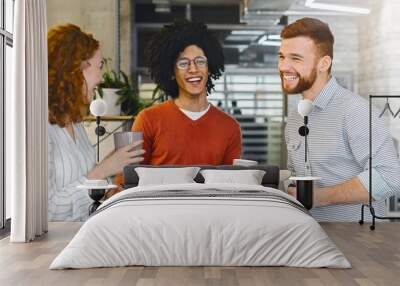 Enjoying free time. Group of millennial coworkers drinking coffee and talking in modern coworking space Wall mural