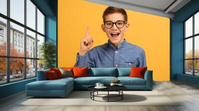 Enthusiastic teen boy wearing glasses pointing upwards with finger Wall mural