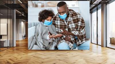 Epidemic hygiene strategies. African American family wearing protective masks and cleaning hands with sanitizer indoors Wall mural