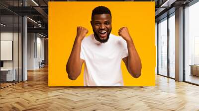 Excited african-american man shakes clenched fists at studio Wall mural