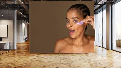 Excited african american woman taking off hydrogel eye patches, standing isolated on brown background, free space Wall mural