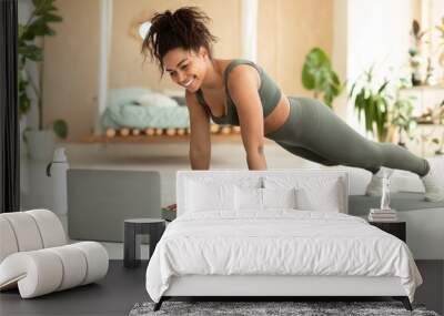 Excited athletic african american lady exercising at home, sporty black woman enjoying online yoga class, using laptop Wall mural