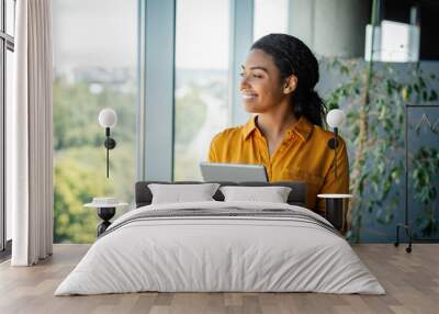 Excited black businesswoman standing in modern coworking office room, looking through window, copy space Wall mural