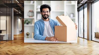 Excited indian man opening delivery box while sitting at desk at home Wall mural