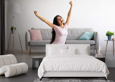 Excited Indian woman sitting on scales, raising hands up, happy with result of her weight loss program at home Wall mural