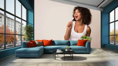 Excited lady eating healthy salad over light background Wall mural