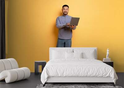 Excited Young Asian Man With Laptop Computer Posing Over Yellow Studio Background Wall mural