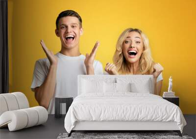 Excited young people rejoice success, exclaiming with triumph, standing next to each other on yellow background Wall mural