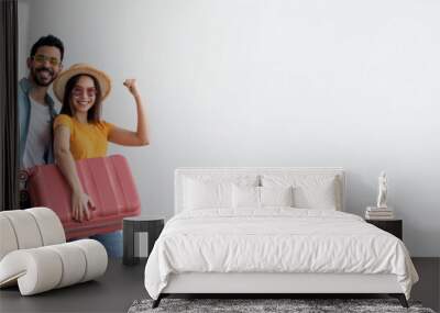 Family tours concept. Happy young couple with suitcase, passports and tickets posing over light wall and smiling at camera. Diverse tourists spouses ready for vacation trip, full length, copy space Wall mural