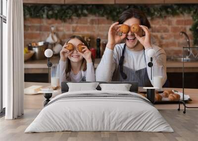 Father and daughter having fun in kitchen, making cupcake eyes Wall mural