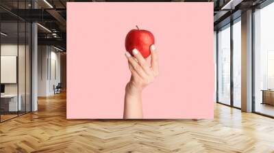 Female hand holding ripe red apple on pink background, close up. Panorama Wall mural