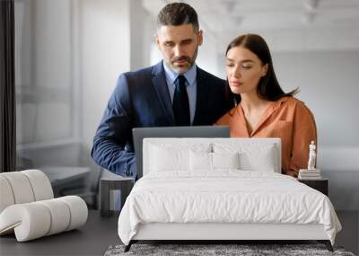 Female manager talking with experienced male colleague while using laptop computer together in office Wall mural