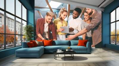 Five colleagues gather around a table in an office, discussing and collaborating on a project using documents and a tablet. Wall mural