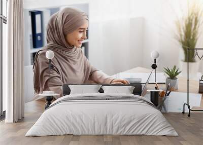 Focused arabic businesswoman in hijab working on laptop computer in office Wall mural