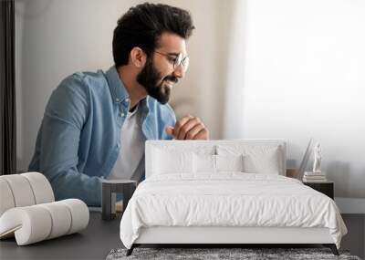 Focused indian man looking at laptop screen and writing in notebook Wall mural