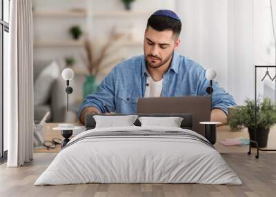 Focused israeli man working on laptop amd writing at home Wall mural