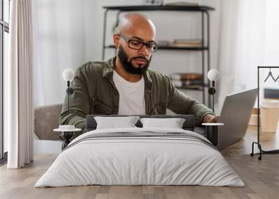 Focused mature latin man taking notes while using laptop, working or learning distantly online, sitting at desk at home Wall mural