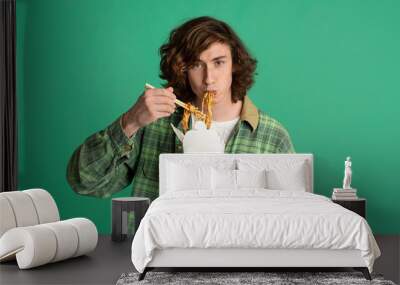 Food delivery concept. Young man eating takeaway noodles on color background, blank space for design Wall mural