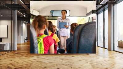 Friendly black female teacher checking off children names sitting inside school bus Wall mural