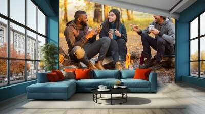 Friends sitting beside fireplace in autumn forest, enjoying time together Wall mural