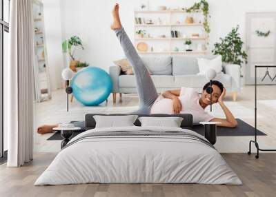 Full length portrait of expectant black woman exercising on yoga mat, lifting her leg up, feeling healthy at home Wall mural