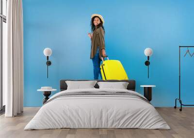 Full length portrait of happy black female traveler walking with suitcase over blue studio background, copy space Wall mural