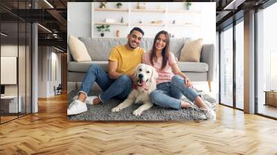 full length portrait of positive international couple with their pet dog sitting on soft carpet at h Wall mural