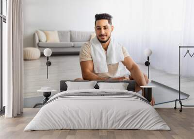 Full length portrait of sporty young Arab man holding bottle of water during his workout at home Wall mural