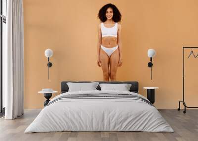 Full length portrait of young black slender lady with perfect body shape and flat tummy posing on beige background Wall mural