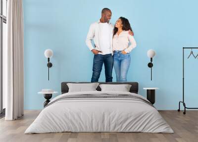 Full length shot portrait of black couple hugging and looking at each other, posing on blue background, full body length Wall mural