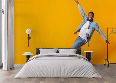 Funny black guy posing on tiptoes over yellow background in studio Wall mural