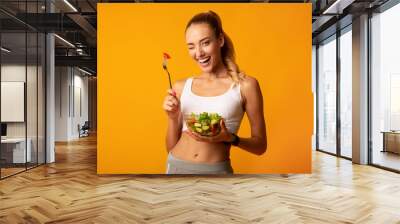 Girl Eating Salad Winking At Camera Over Yellow Background Wall mural