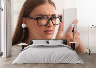 Girl Squinting Eyes Looking At Smartphone Through Eyeglasses Sitting Indoor Wall mural