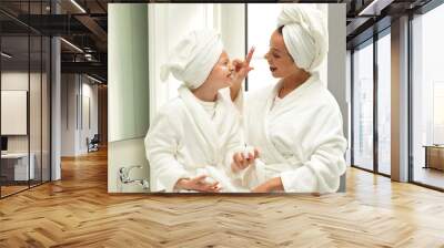 Glad caucasian teen and young mom in bathrobe and towel, have fun, apply cream, enjoy beauty care Wall mural