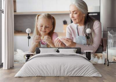 Glad european little girl and old grandmother in aprons make cookies from dough, sculpt dumplings Wall mural