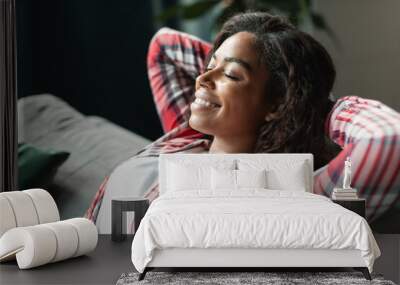 Glad happy pretty black young female with closed eyes resting alone on sofa, enjoys silence and comfort Wall mural