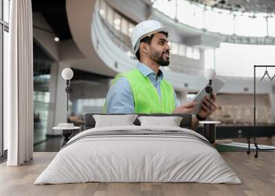 Glad millennial middle eastern man engineer in protective uniform and hardhat with beard hold tablet Wall mural