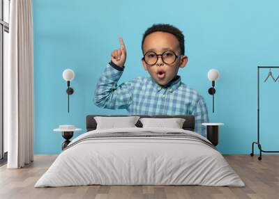 Great idea. Emotional black boy in eyeglasses pointing finger up and looking at camera, posing over blue background Wall mural