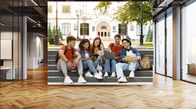 Group Of Students With Digital Tablet And Laptop Study Together Outdoors, Happy Multiethnic Young Friends Sitting On Stairs Near University Building, Using Modern Gadgets For Education, Copy Space Wall mural