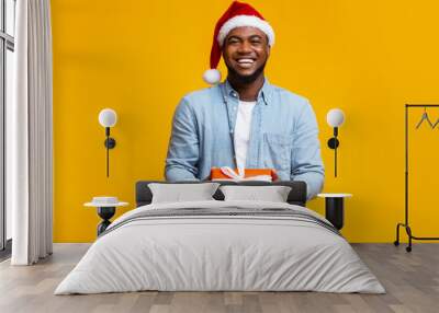 Handsome black guy in red Santa hat holding gift box Wall mural