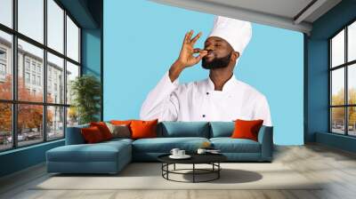 handsome black male chef in uniform kissing fingers, standing over blue background Wall mural