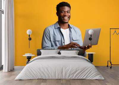 Handsome black man using modern laptop on yellow Wall mural