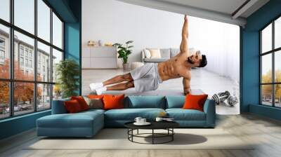 Handsome young Arab man standing in side plank on yoga mat at home, copy space Wall mural