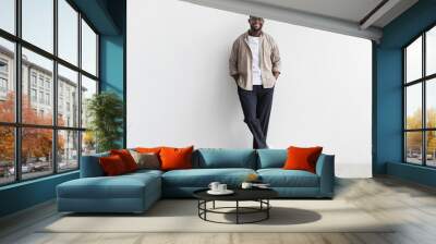 Handsome young black man in casual wear looking at camera and smiling, standing against white studio wall, copy space Wall mural