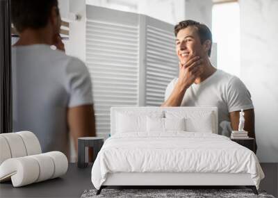 Handsome young man looking in the mirror, touching chin Wall mural