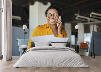 Happy african american businesswoman having phone call with business partner, holding papers, working in office Wall mural