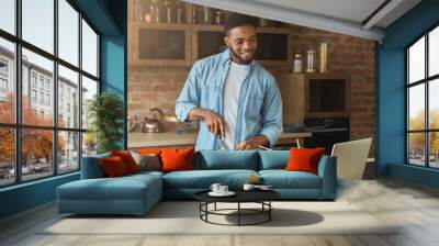 Happy african-american man preparing salad in kitchen Wall mural