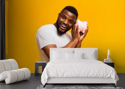 Happy african american man shaking full piggy bank Wall mural